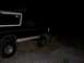 1992 Ford Bronco - A 1992 Ford Bronco is parked on a gravelly incline at night, with its headlights on.