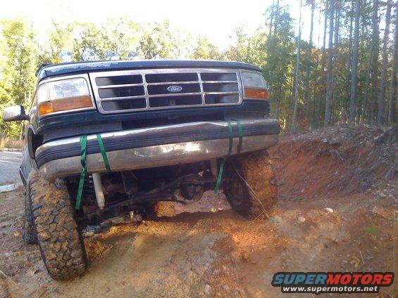 Dark green Ford truck with off-road tires on a dirt trail, front view