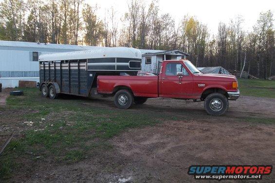 Red 1987 Ford F-250 pickup truck towing a black and white trailer, viewed from the side