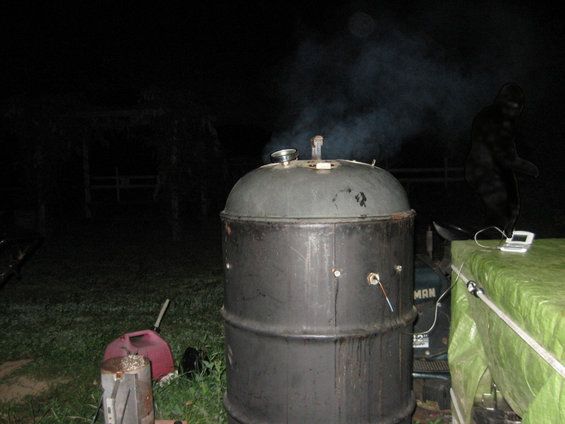 Outdoor smoker with smoke rising, next to a green tarp-covered surface with a small electronic device
