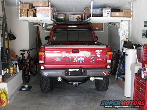1999 Ford Ranger pickup truck parked in a garage, rear view. Truck has many stickers on the tailgate