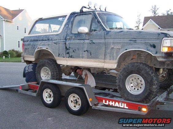 Ford Bronco on a U-Haul trailer with two people working underneath it