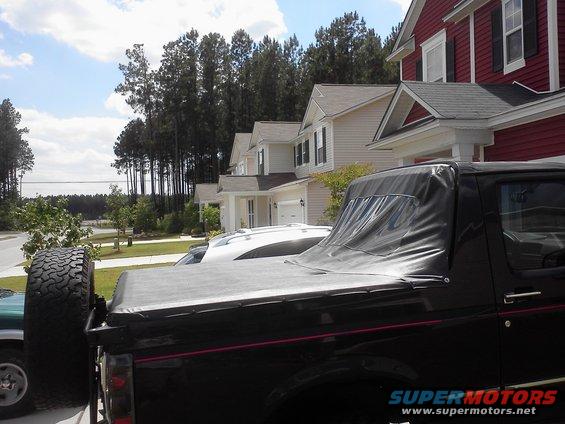 Black 1992 Ford Bronco with a soft top, spare tire mounted on the rear, and a red stripe along the side