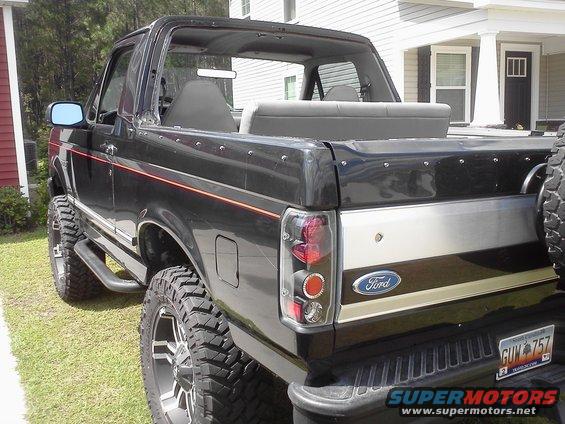 Black Ford Bronco with orange stripe, lifted with big tires. Rear view shows Ford emblem and custom taillights