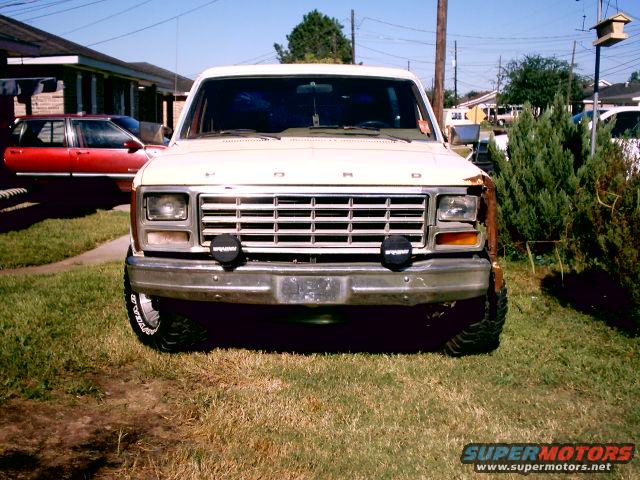 Front view of a white 1980 Ford Bronco with a red car in the background