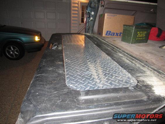 Truck bed with diamond plate cover, green sedan in background