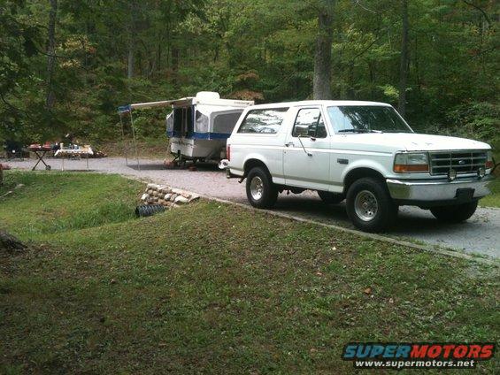 White 1992 Ford Bronco towing a pop-up camper at a campsite