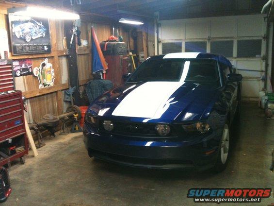 Blue 2010 Ford Mustang with white racing stripes parked in a garage