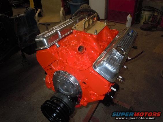 Orange V8 engine block with chrome valve covers and a pulley system