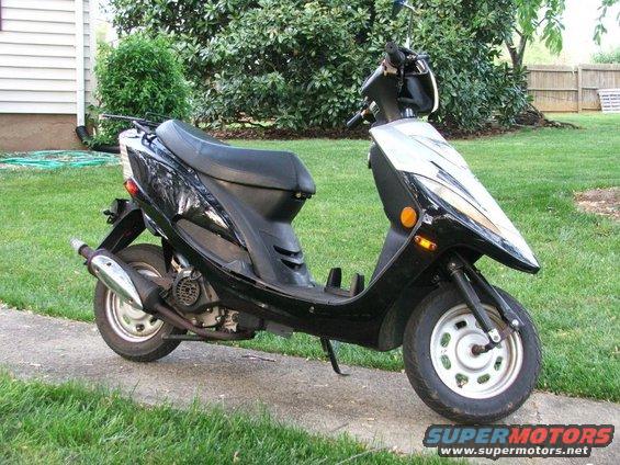 Black scooter parked on a concrete path in front of a house and trees