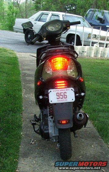 Black scooter rear view, license plate 956 MOPED, with two cars in background