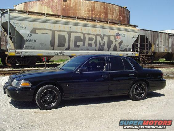 Black sedan parked next to a train car. The car has aftermarket wheels