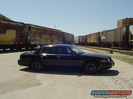 Black 1999 Ford Crown Victoria parked by train cars