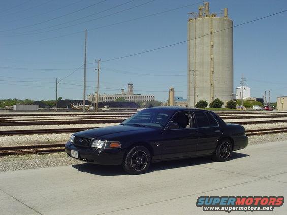 Black sedan parked on concrete near railroad tracks with industrial buildings in background