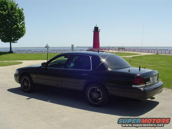 Black sedan parked on pavement with a red lighthouse and water in the background