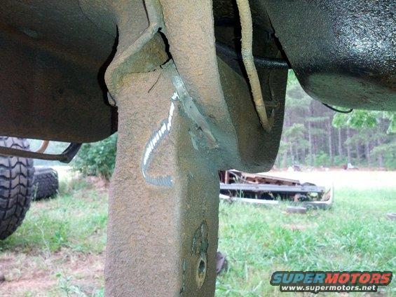 Close-up of rusty, modified vehicle frame with visible welds and a large tire in the background