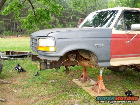 Ford F-350 truck with mismatched front fenders, raised on jack stands, with red and tan doors