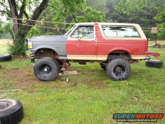 Red and gray Ford Bronco with lifted suspension and large tires, parked on grass