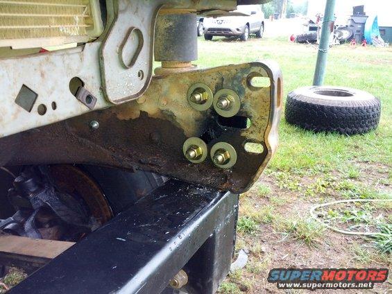 rusted frame bracket with four bolts and washers, spare tire and SUV in background