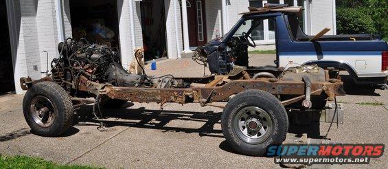 Ford Bronco chassis with engine and transmission removed, body partially intact, sitting outside a garage