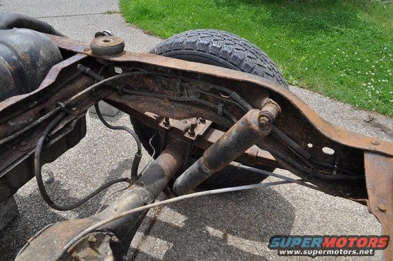 Rusted frame section with rear axle, shocks, and fuel tank. Tire visible