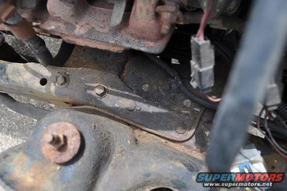 Engine bay close-up showing rusty metal brackets, bolts, and electrical connectors