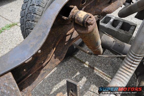 Close-up of rusty vehicle frame, shock absorber, and tire. Shows part of the suspension system
