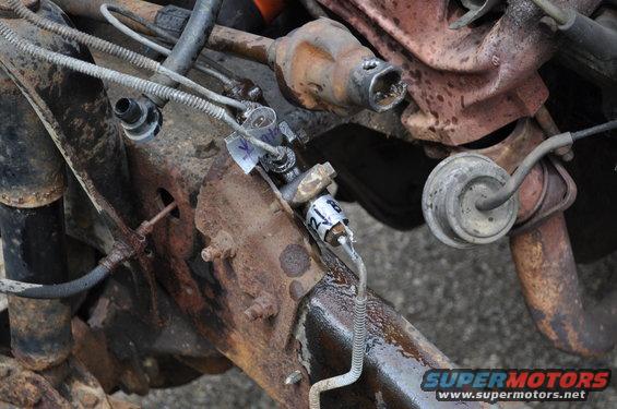 Close-up of rusty vehicle frame with brake lines and engine parts. A tag reads '21B'
