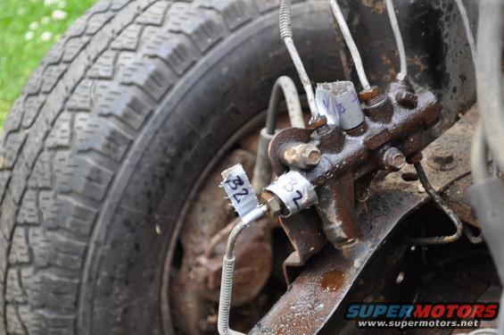 Close-up of a brake master cylinder with tape labels 'B2' and 'V' next to a tire