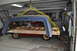 1986 Ford Bronco - Car body and camper shell suspended by straps in a garage during a teardown process.