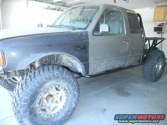 Gray Ford Ranger truck with aftermarket roll cage and large off-road tires, front fender is unpainted