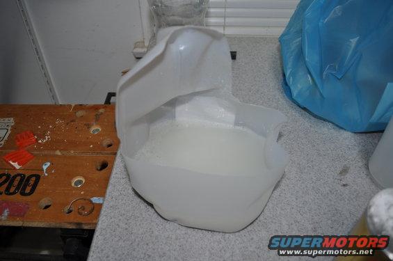 Plastic jug with white liquid on a counter next to a blue bag and a wooden surface with numbers