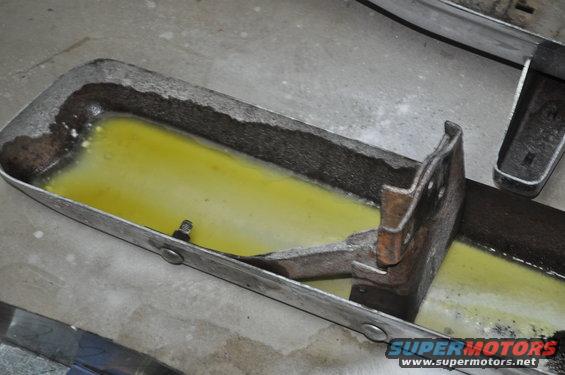 Metal part filled with yellow liquid, showing rust and damage