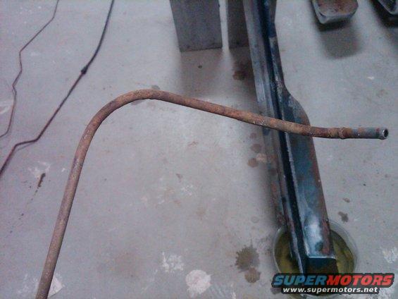 rusted metal tube bent over a dark frame piece on a concrete floor