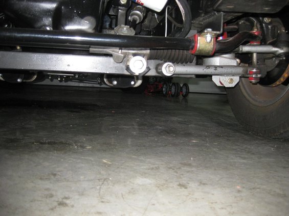 Underside view of a car's steering and suspension components. A red dolly with wheels is visible under the front
