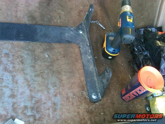 Metal bracket with bolts, a cordless drill, and a cup with 'DENVER' text on a carpeted surface