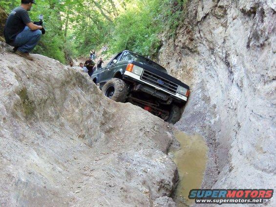 Ford Bronco II going down a steep, muddy trail with people watching