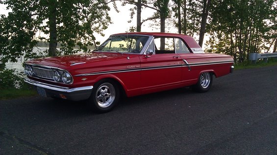 Red 1963 Ford Falcon parked by a lake with trees