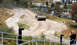 2012 Ford Bronco - An armored personnel carrier navigates a dirt path near a modern office building and parking lot.