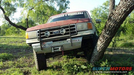 Red and silver Ford truck with winch, off-roading near a tree