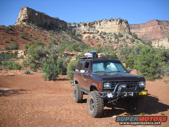 Brown 1986 Ford Bronco II with off-road tires and roof rack parked in desert landscape
