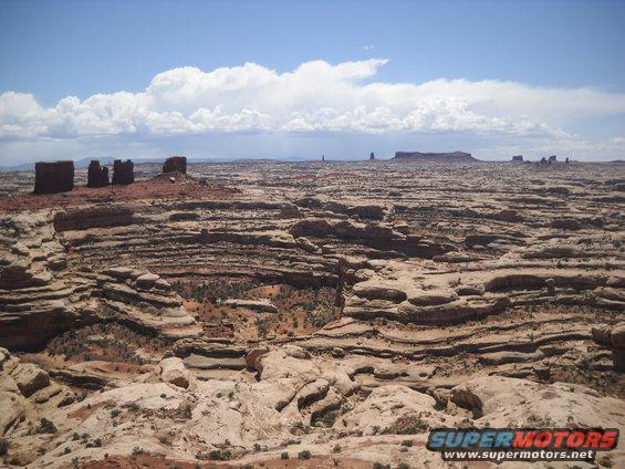 Desert landscape with layered rock formations and mesas under a cloudy blue sky
