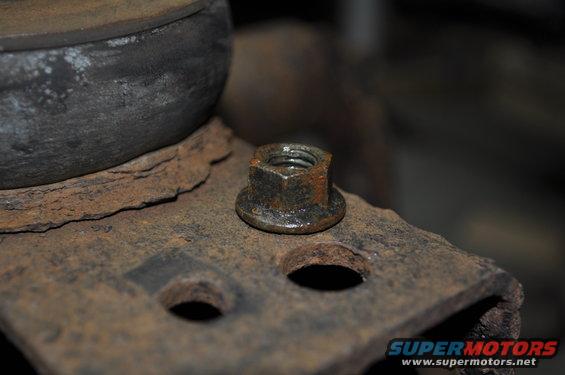 Close-up of a rusted nut on a metal bracket, with a dark, out-of-focus background