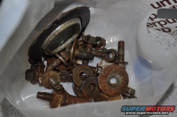 Pile of rusty bolts, washers, and a black rubber gasket in a plastic bag