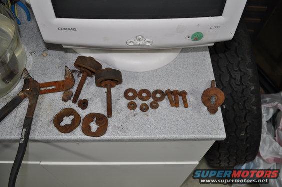 Rusty bolts, washers, and what appear to be brake caliper parts laid out on a counter next to pliers and a computer monitor