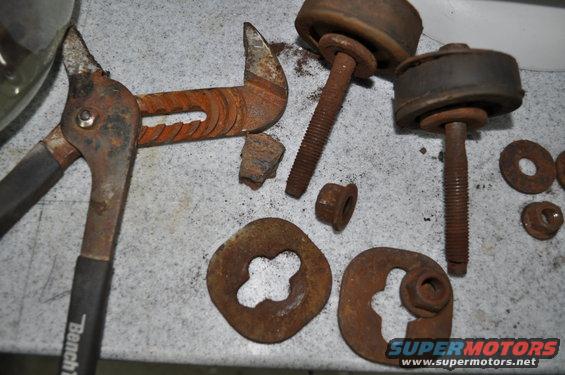 Rusty pliers, bolts, washers, and chunks of metal on a speckled surface. One bolt has a rubber bushing attached