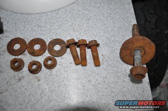 Rusty bolts and washers on a speckled surface, with a tire visible on the right