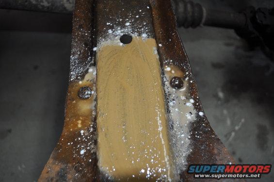Close-up of a rusty metal bracket being cleaned with a brown solution and white droplets
