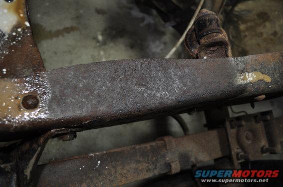 Rusted frame rail with visible bolts and yellow fluid drip