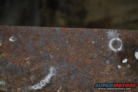 Close-up of a heavily rusted metal surface with some white residue and a circular mark